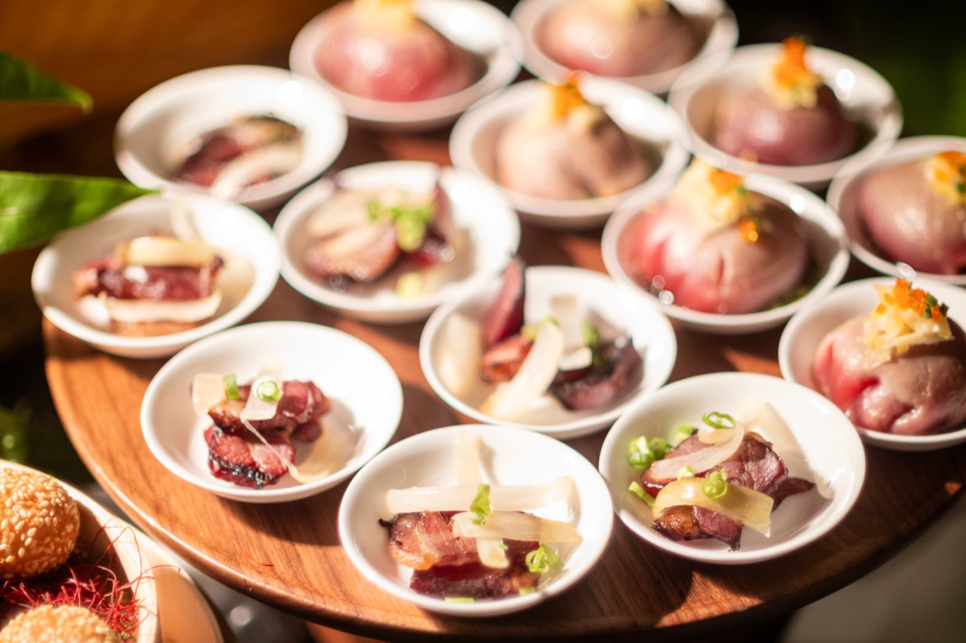 Small white bowls of cured meat and raw fish appetizers on a wooden serving tray